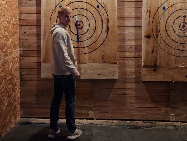 Image of a teen posing for a photo at Smoke Eaters Axe Throwing lanes - Image of two individuals throwing axe on their target at Smoke Eaters Axe Throwing - https://smokeeatersnd.com/