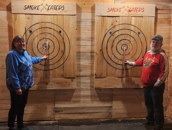 Image of two elderly adults posting for a photo at Smoke Eaters axe throwing lane targets - Image of two individuals throwing axe on their target at Smoke Eaters Axe Throwing - https://smokeeatersnd.com/